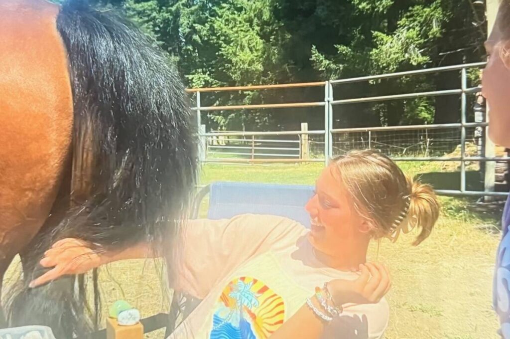 Person sitting near a horse outdoors.